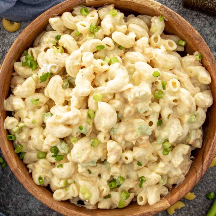 Creamy Hawaiian macaroni salad in a wooden bowl garnished with sliced green onions, set on a gray textured surface.