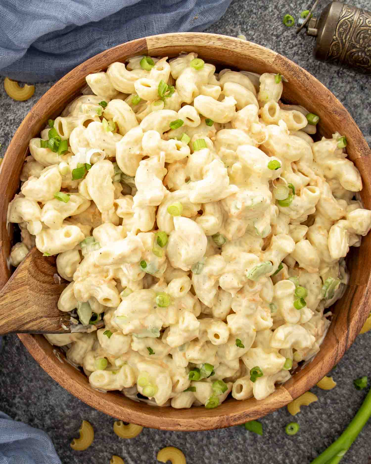 Creamy Hawaiian macaroni salad in a wooden bowl garnished with sliced green onions, set on a gray textured surface.