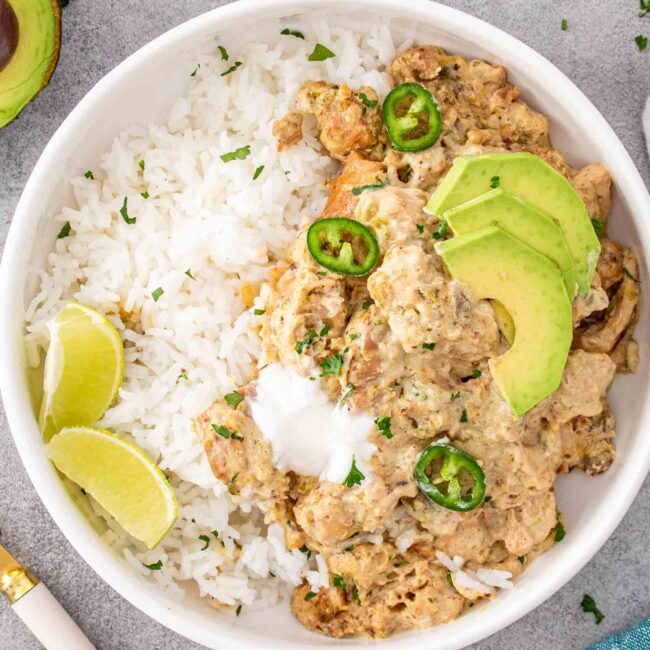 a serving of green chili chicken with rice and avocado in a white bowl.