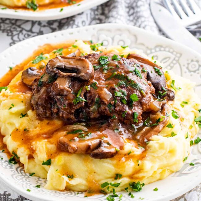 a salisbury steak over a bed of mashed potatoes garnished with parsley.