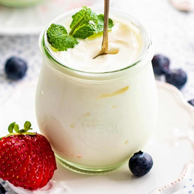 yogurt in a serving jar with a spoon standing garnished with mint and berries.