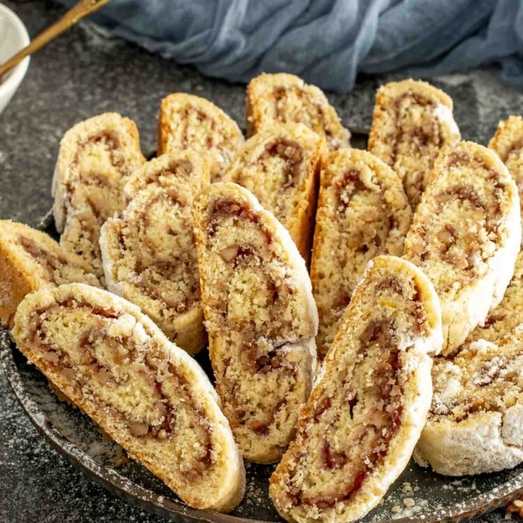 Golden slices of Italian nut roll cookies filled with jam and walnuts, arranged on a tray with scattered walnuts around.