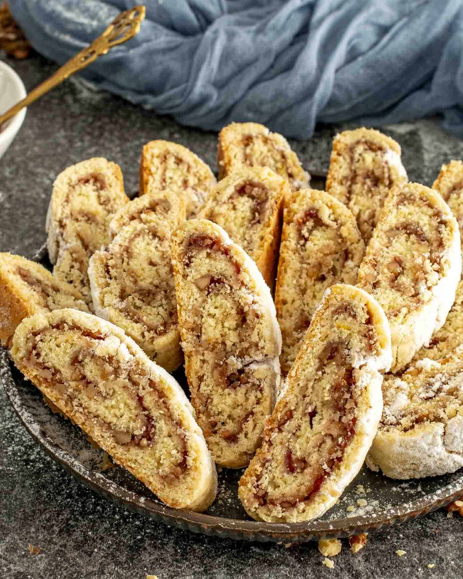 Golden slices of Italian nut roll cookies filled with jam and walnuts, arranged on a tray with scattered walnuts around.