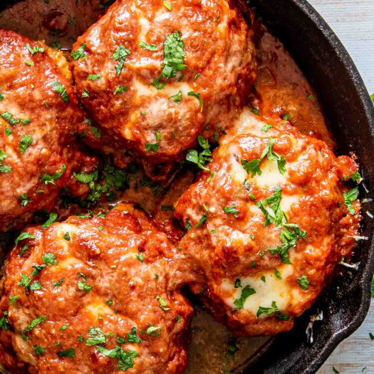 italian style hamburger steak in a cast iron skillet garnished with parsley.