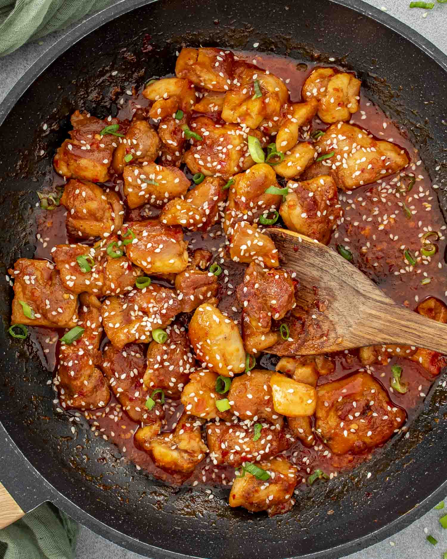 Skillet full of Korean BBQ chicken pieces simmering in thick, glossy red sauce with green onions.