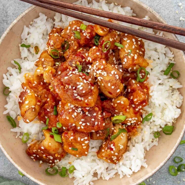Bowl of Korean BBQ chicken and rice with wooden chopsticks resting on the rim, garnished beautifully.