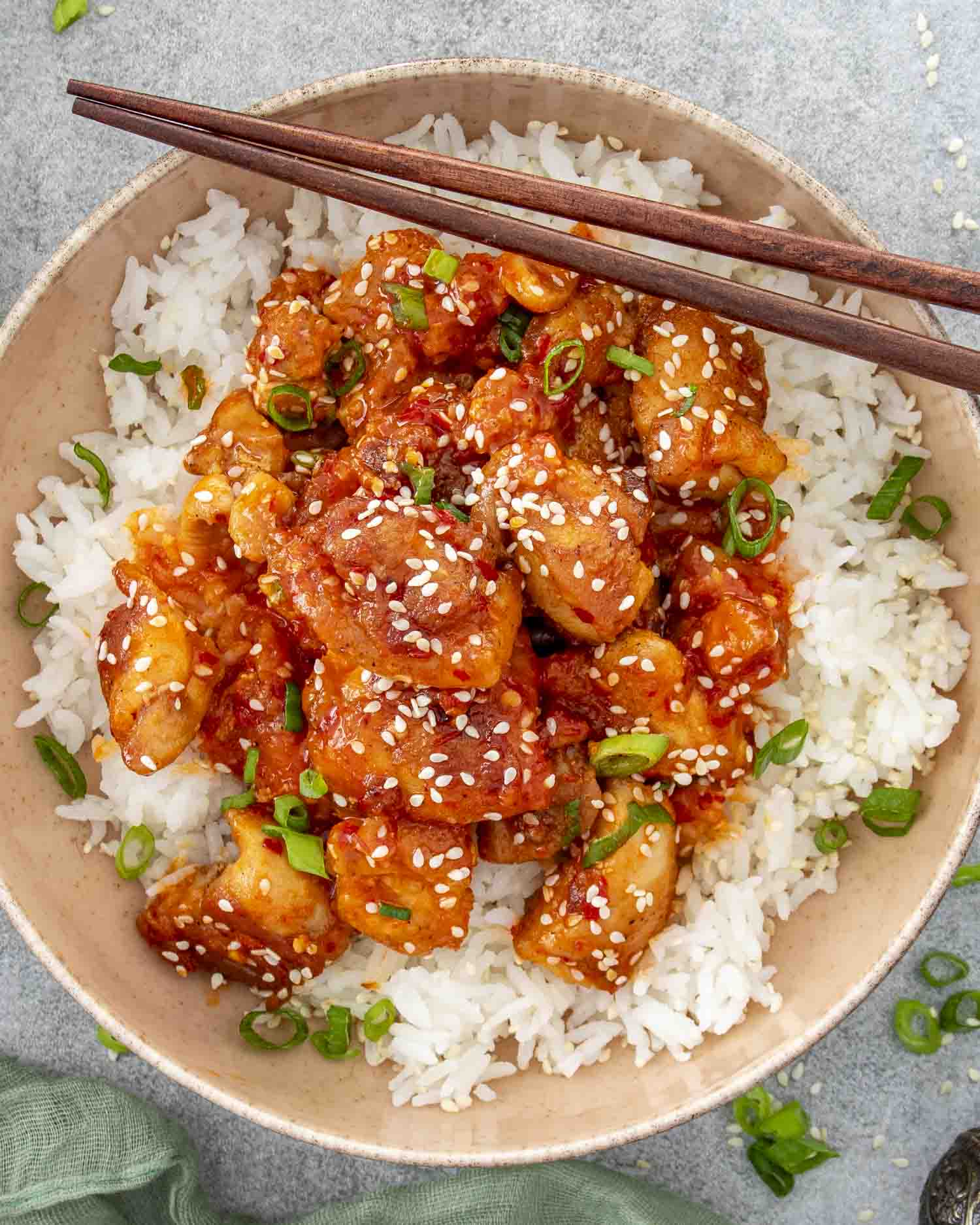 Bowl of Korean BBQ chicken and rice with wooden chopsticks resting on the rim, garnished beautifully.