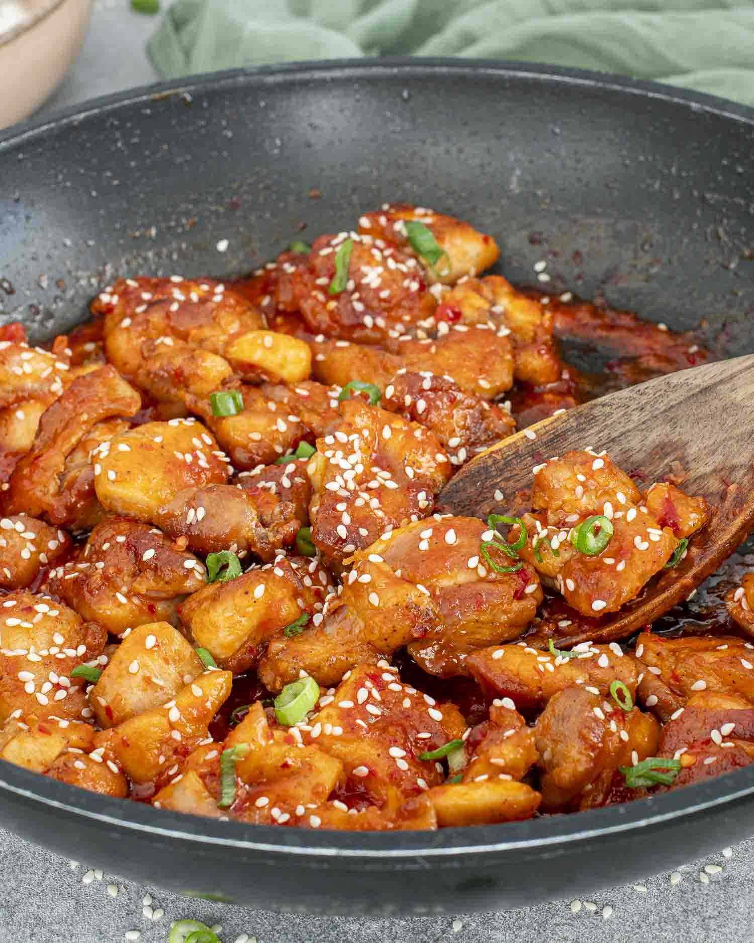 Korean BBQ chicken cooking in a skillet, glistening with sauce and sprinkled with sesame seeds.