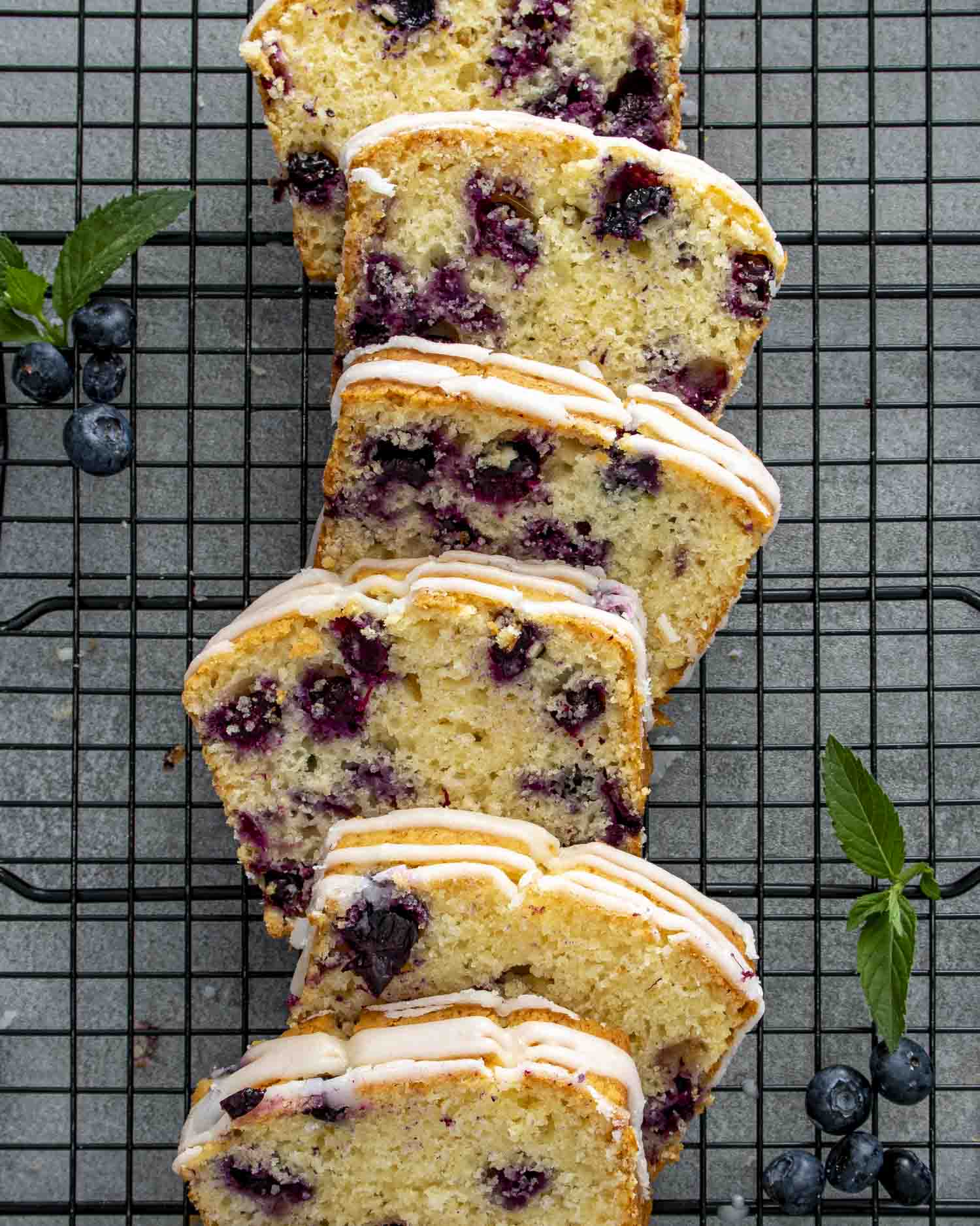 Lemon blueberry bread sliced on cooling rack, showing light texture, golden edges, and generous blueberry distribution throughout each slice.