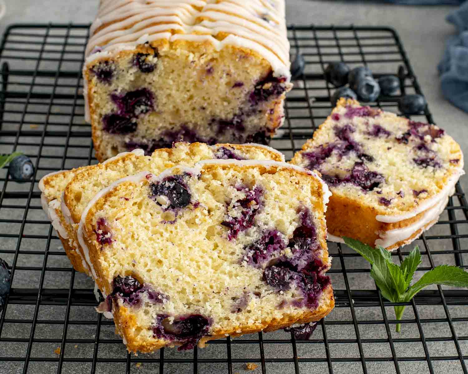 Sliced lemon blueberry loaf cooling on rack, topped with icing drizzle, packed with juicy blueberries and bright lemon flavor.