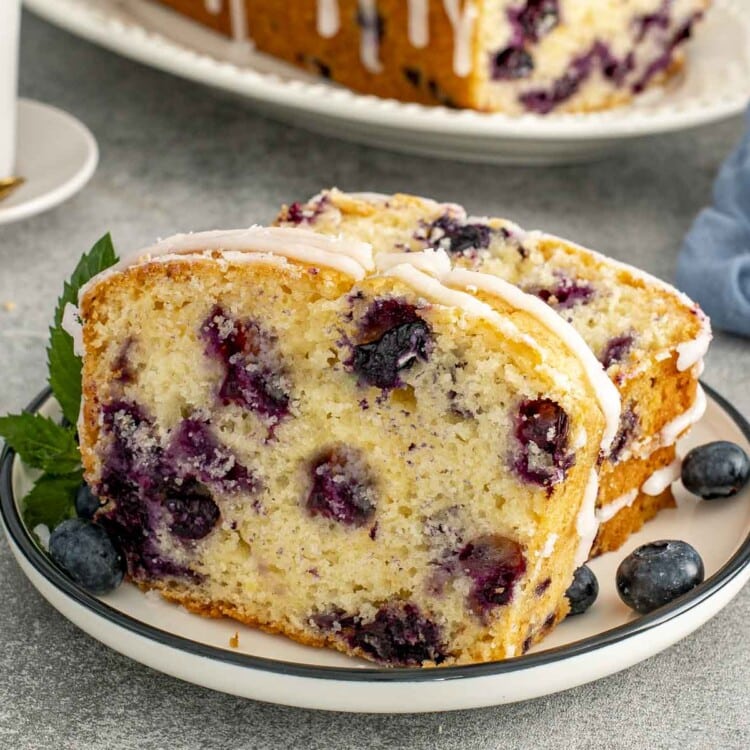 Soft lemon blueberry bread with icing drizzle, sliced and served with fresh blueberries, showing fluffy interior and golden crust.