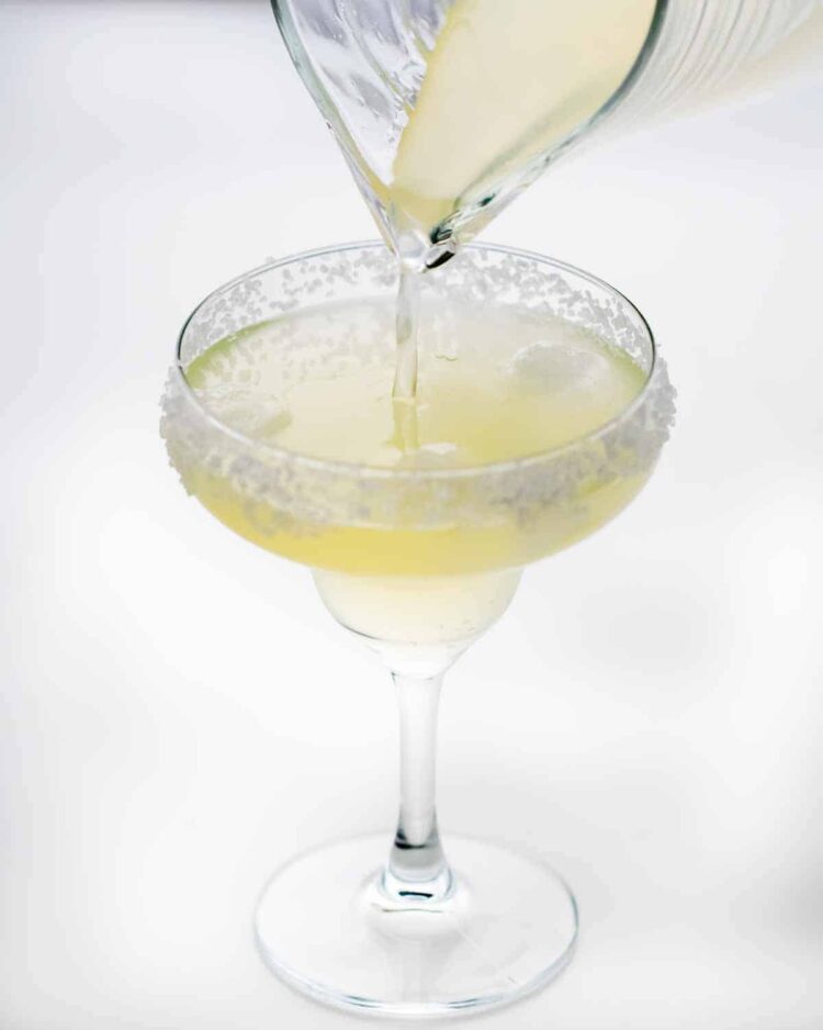 pouring margarita in a rimmed glass