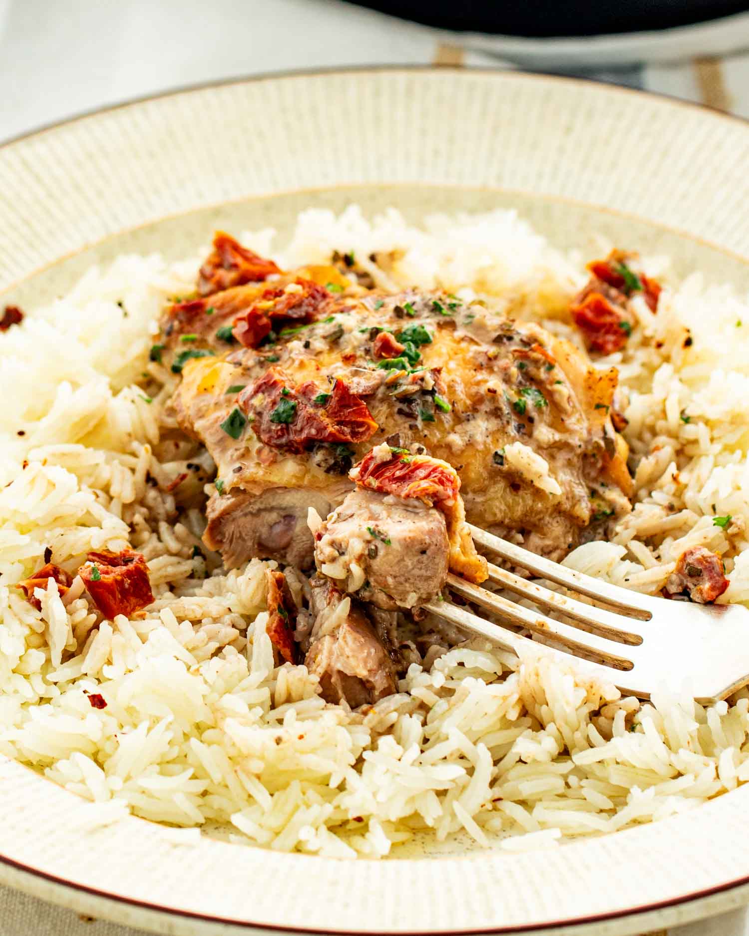 a serving of marry me chicken on a bed of rice in a beige dinner plate.