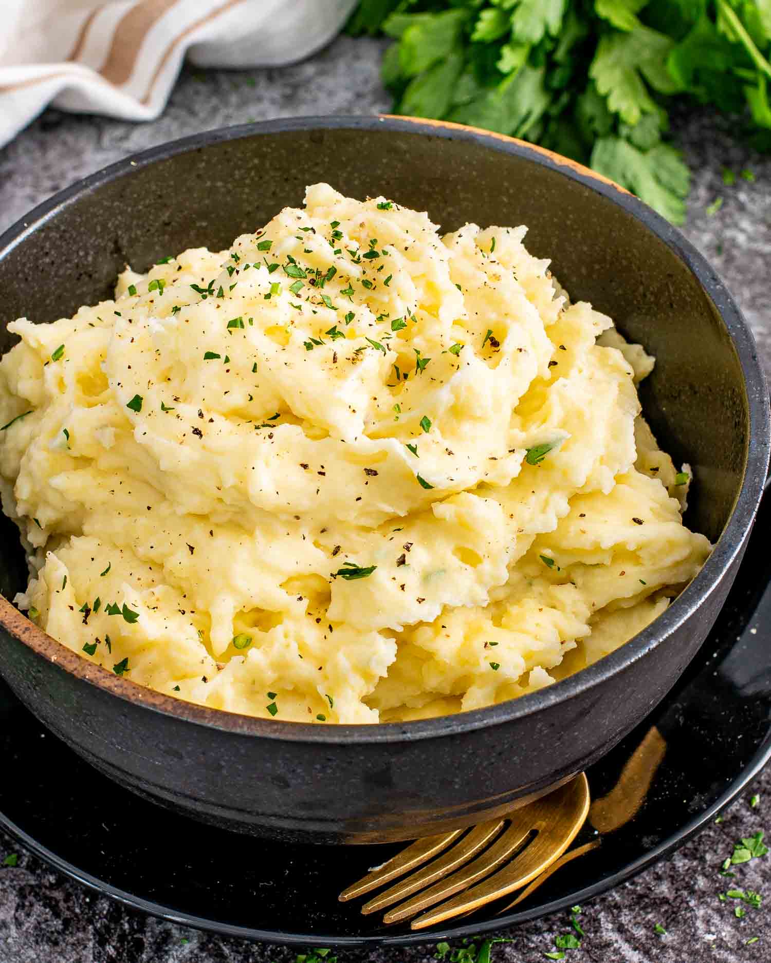 a black bowl loaded with freshly made mashed potatoes garnished with a bit of parsley.