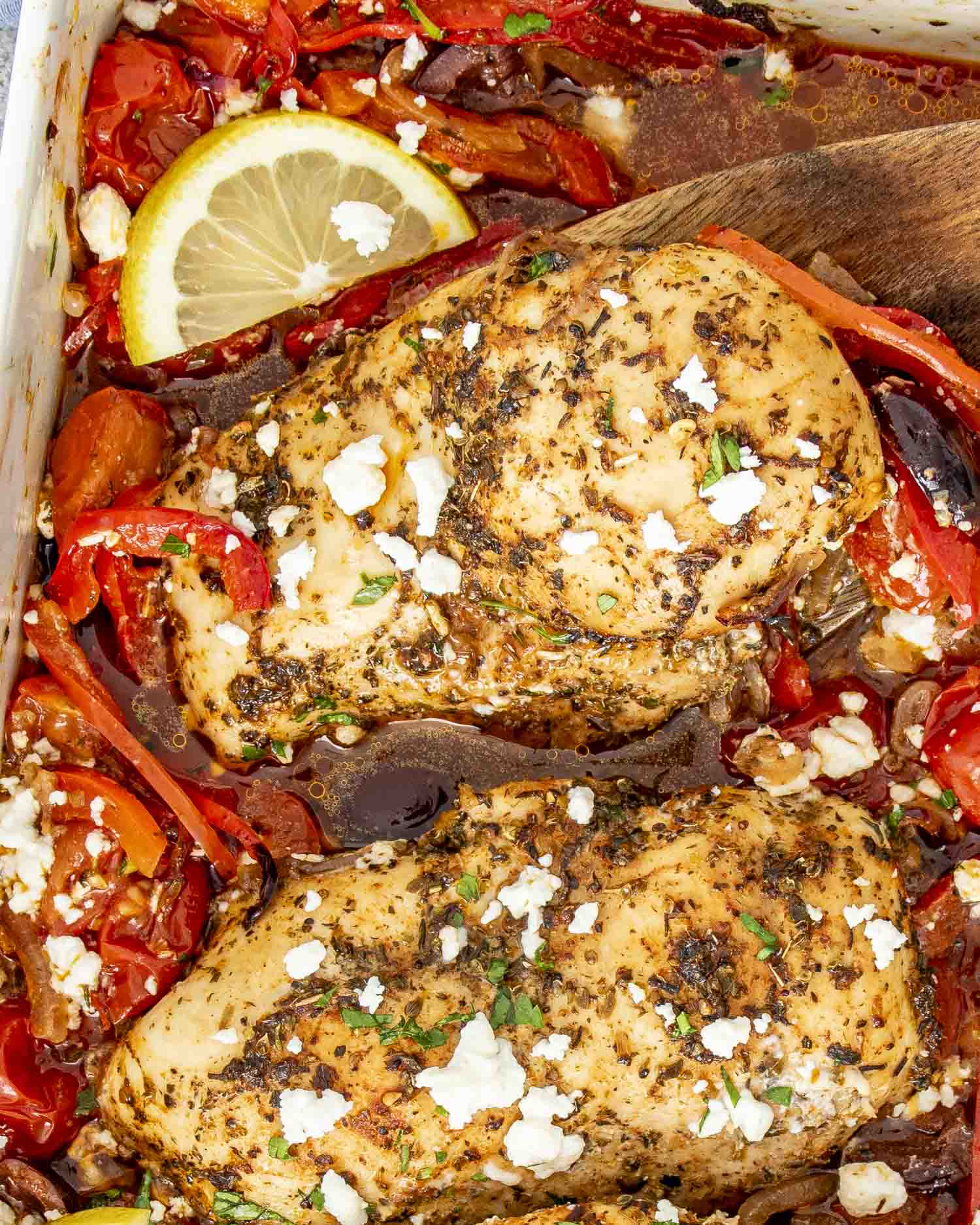 A close-up of Mediterranean Chicken Bake featuring golden-brown chicken breasts seasoned with herbs, nestled among roasted cherry tomatoes, red bell peppers, Kalamata olives, and red onions.