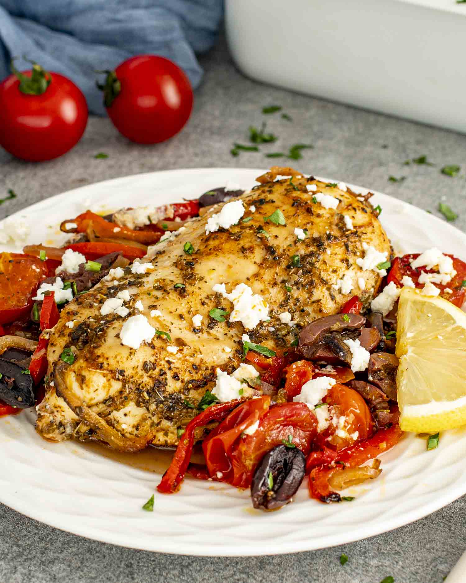 A plate of Mediterranean Chicken Bake showcasing a perfectly cooked chicken breast, seasoned with herbs, and served over a bed of roasted cherry tomatoes, bell peppers, olives, and onions.