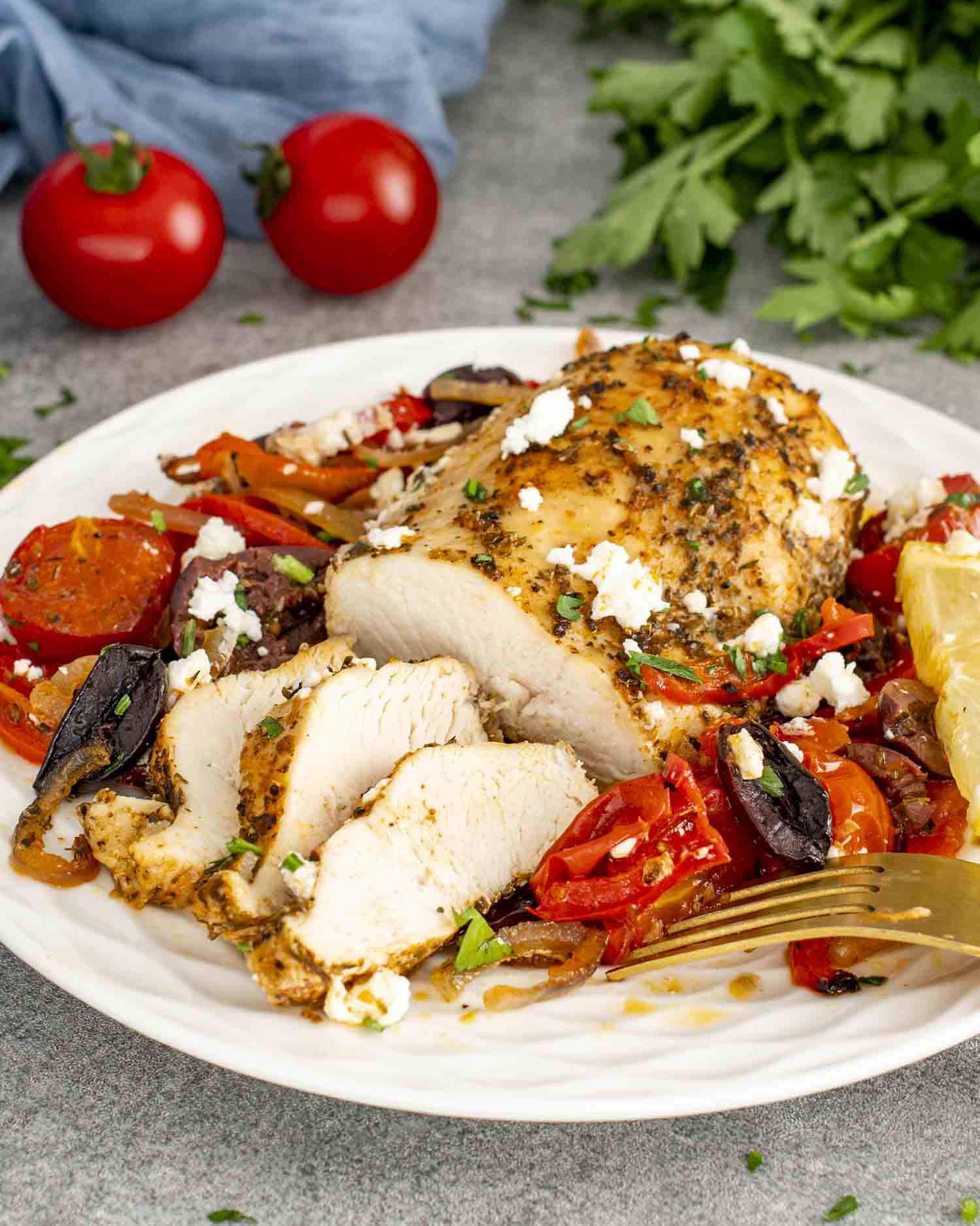 A plate of Mediterranean Chicken Bake showcasing a perfectly cooked chicken breast, seasoned with herbs, and served over a bed of roasted cherry tomatoes, bell peppers, olives, and onions.