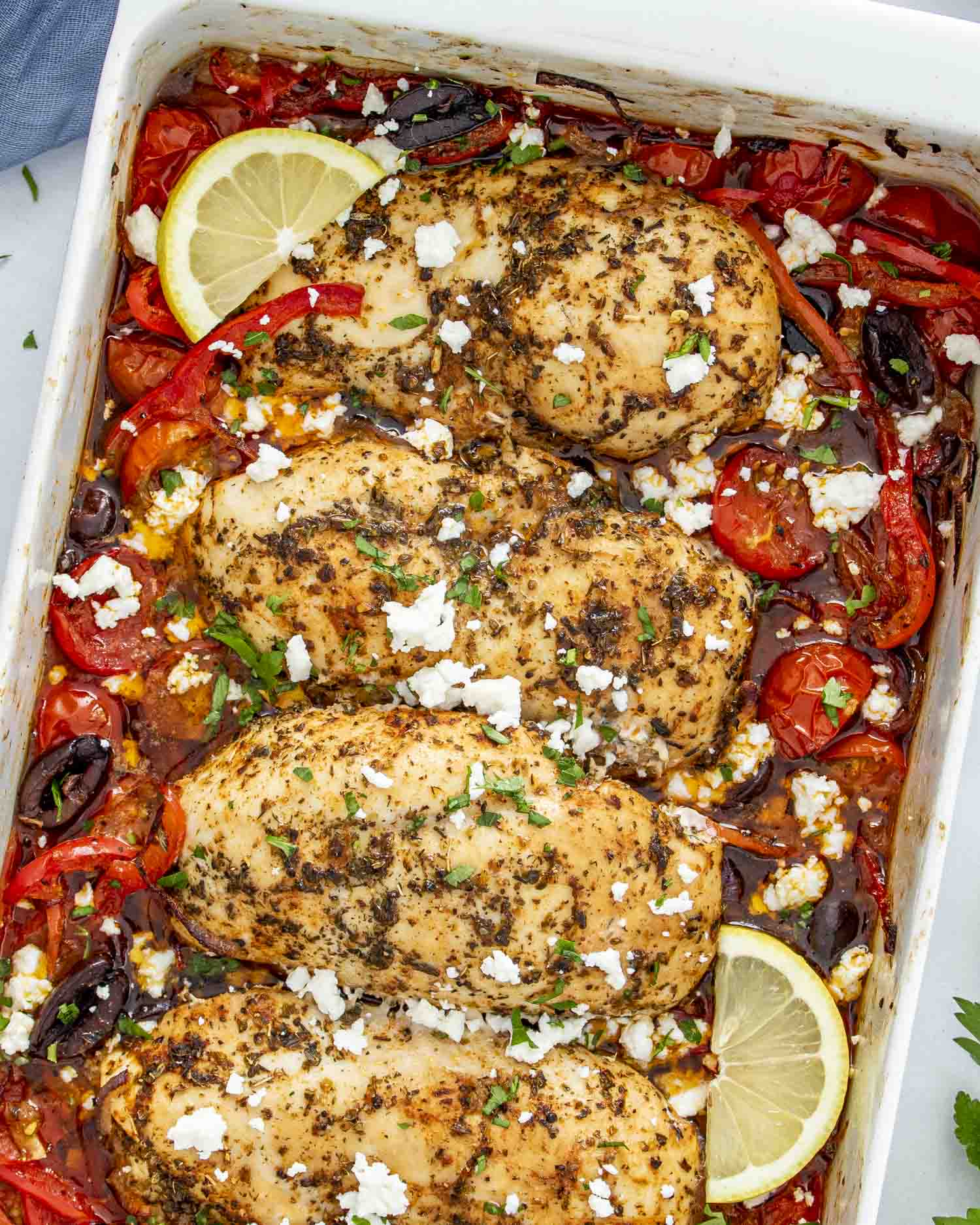A close-up of Mediterranean Chicken Bake featuring golden-brown chicken breasts seasoned with herbs, nestled among roasted cherry tomatoes, red bell peppers, Kalamata olives, and red onions.