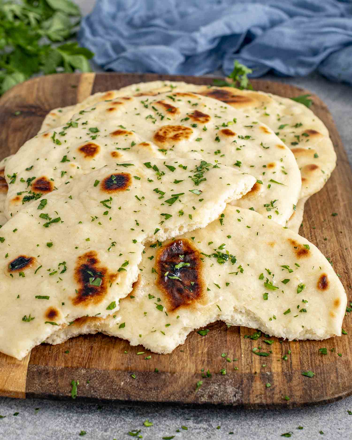 a few scattered naan on a cutting board, brushed with butter and garnished with parsley.