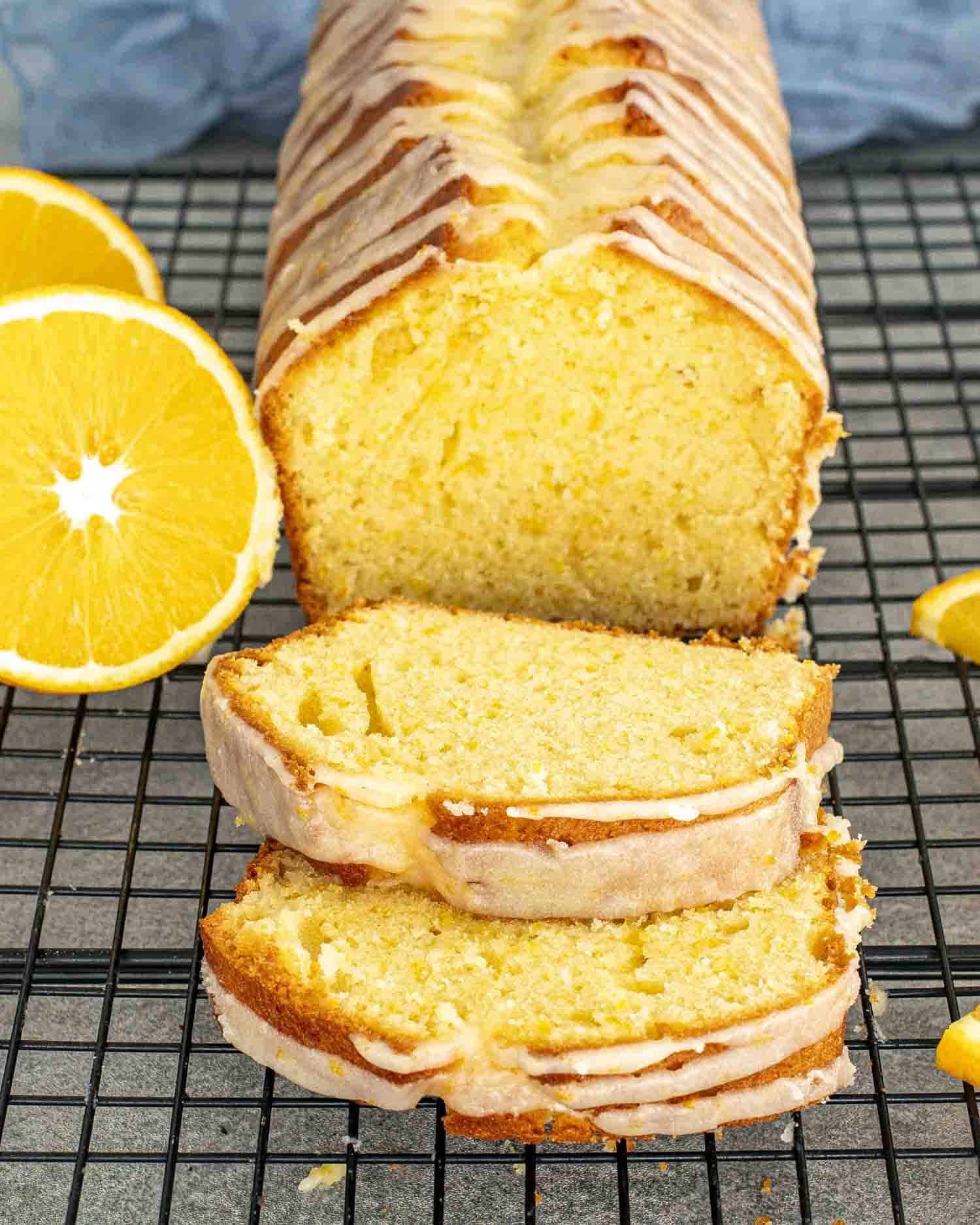 A freshly baked orange cake sliced into thick pieces, drizzled with orange glaze, and resting on a black cooling rack.