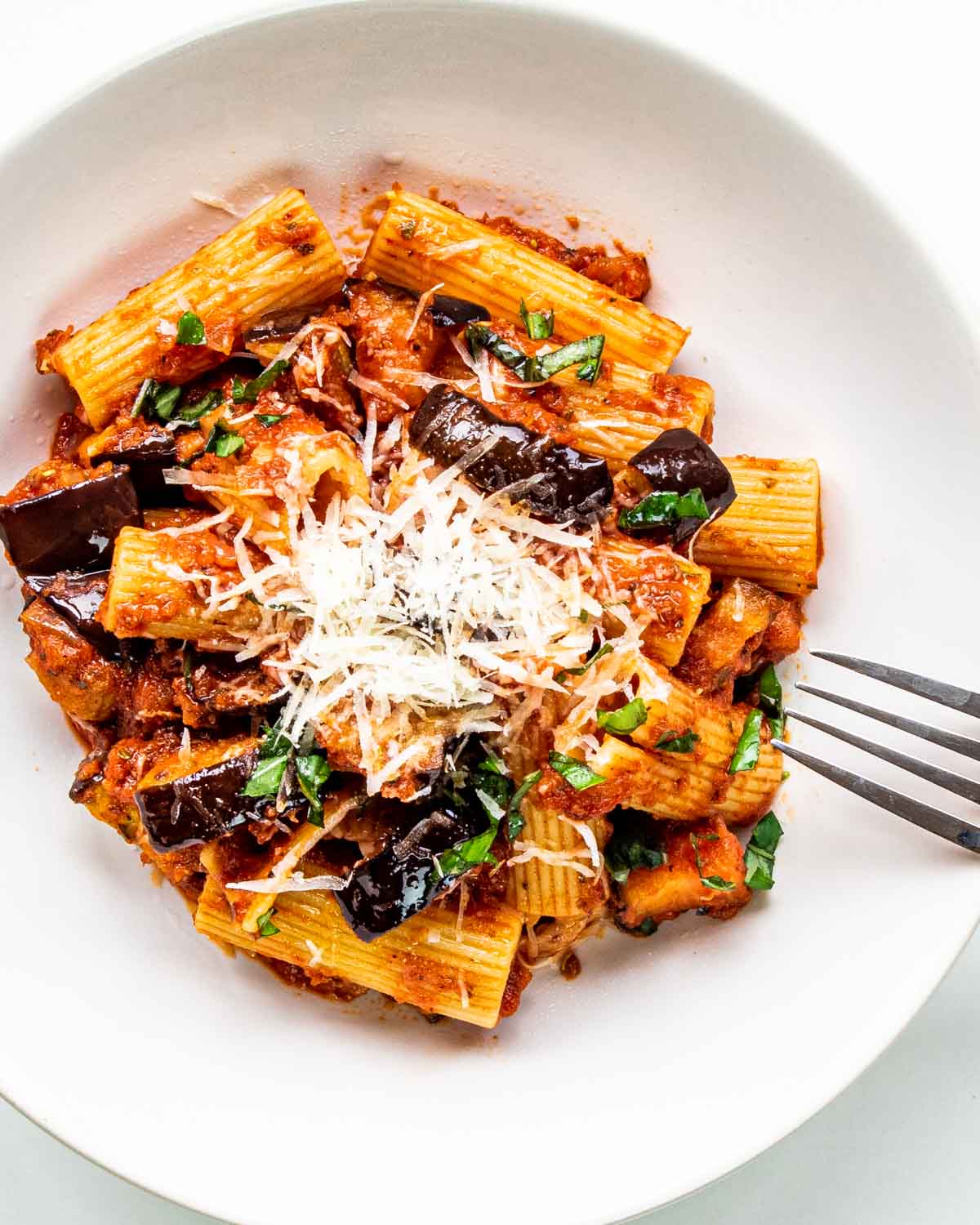 pasta alla norma in a white plate garnished with parmesan cheese.