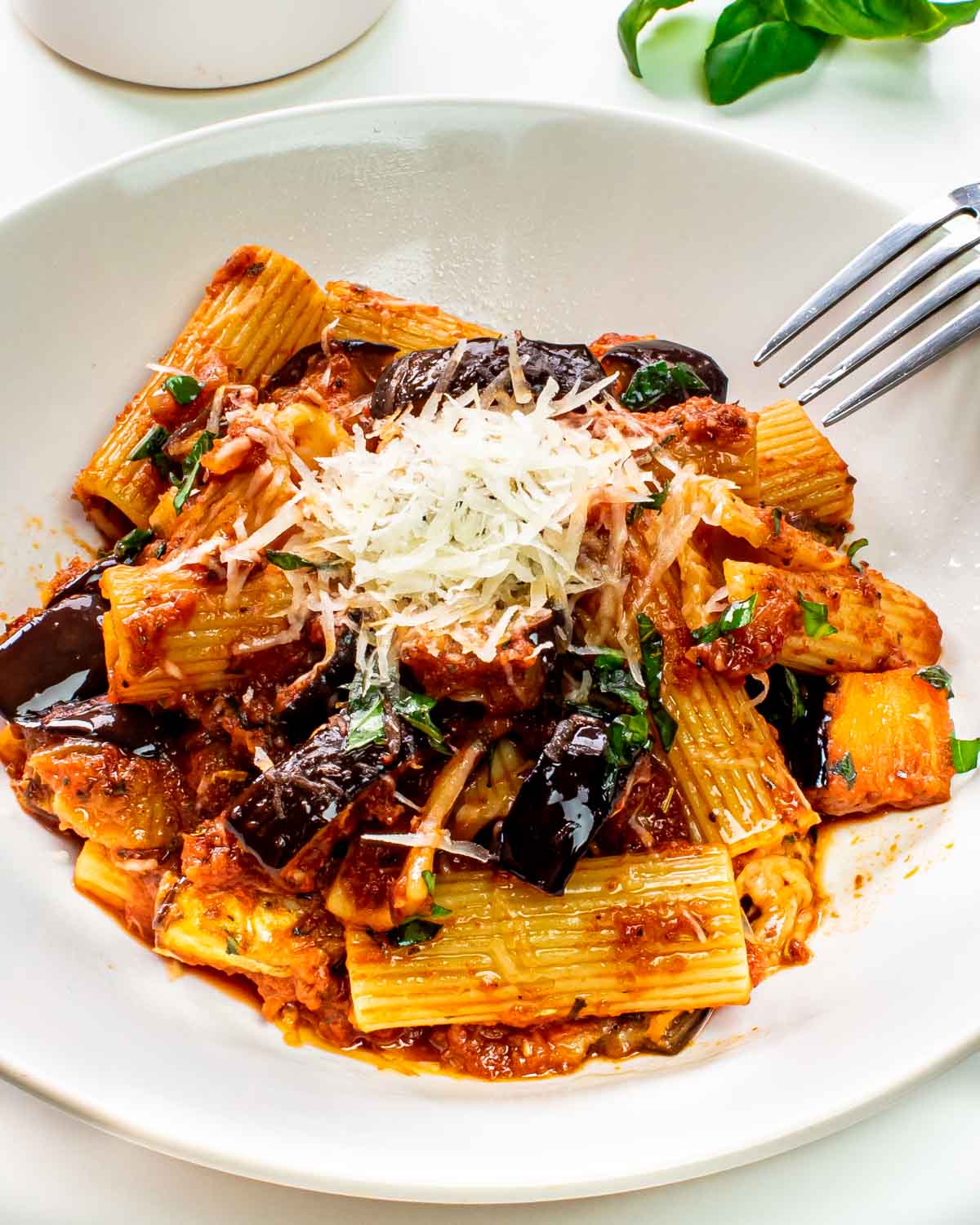 pasta alla norma in a white plate garnished with parmesan cheese.