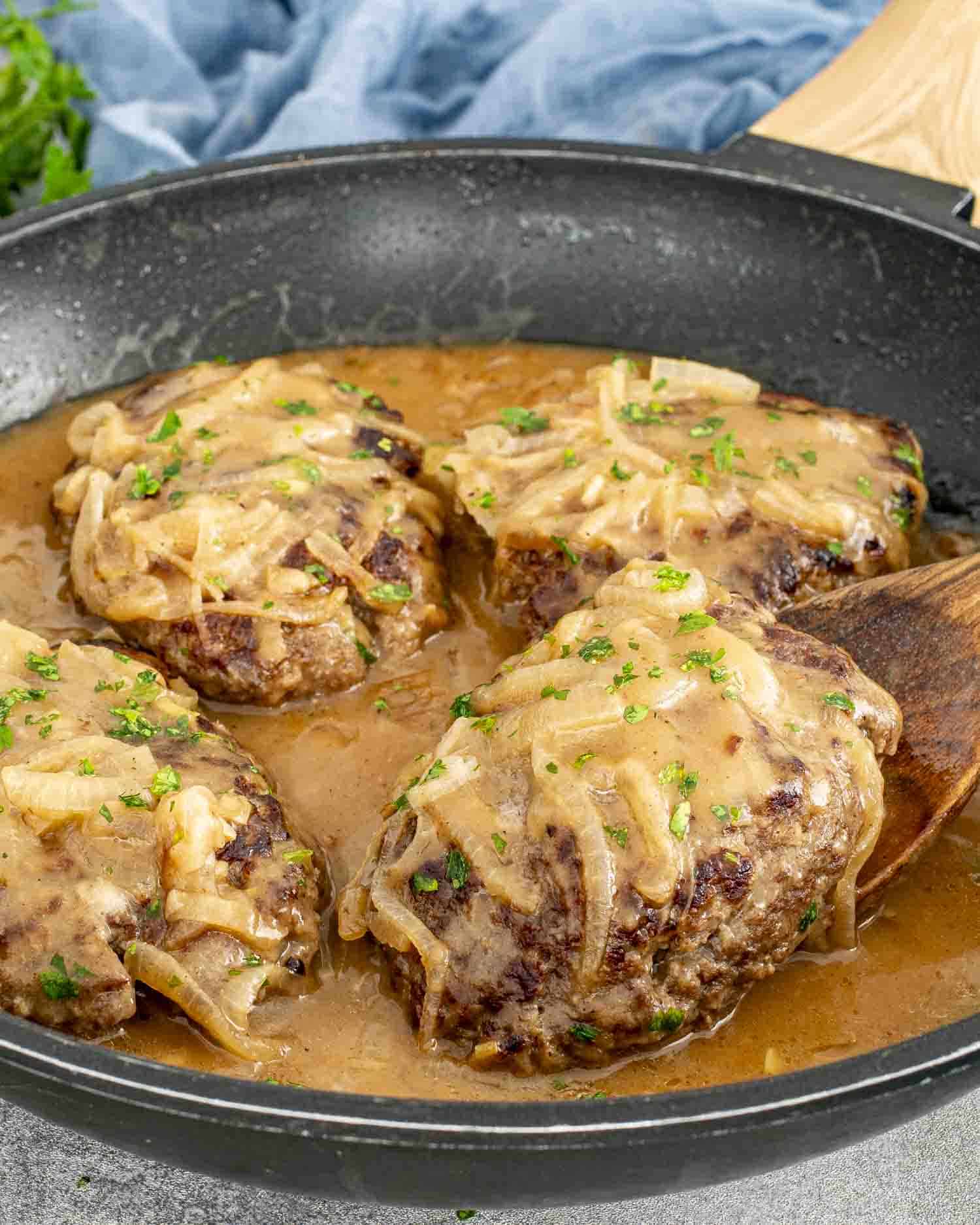 Juicy beef patties covered in rich, creamy onion gravy, garnished with fresh parsley, served hot in a black skillet.