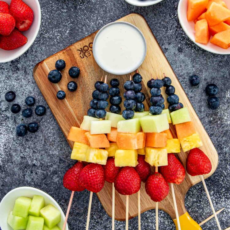 a few rainbow fruit skewers on a cutting board.