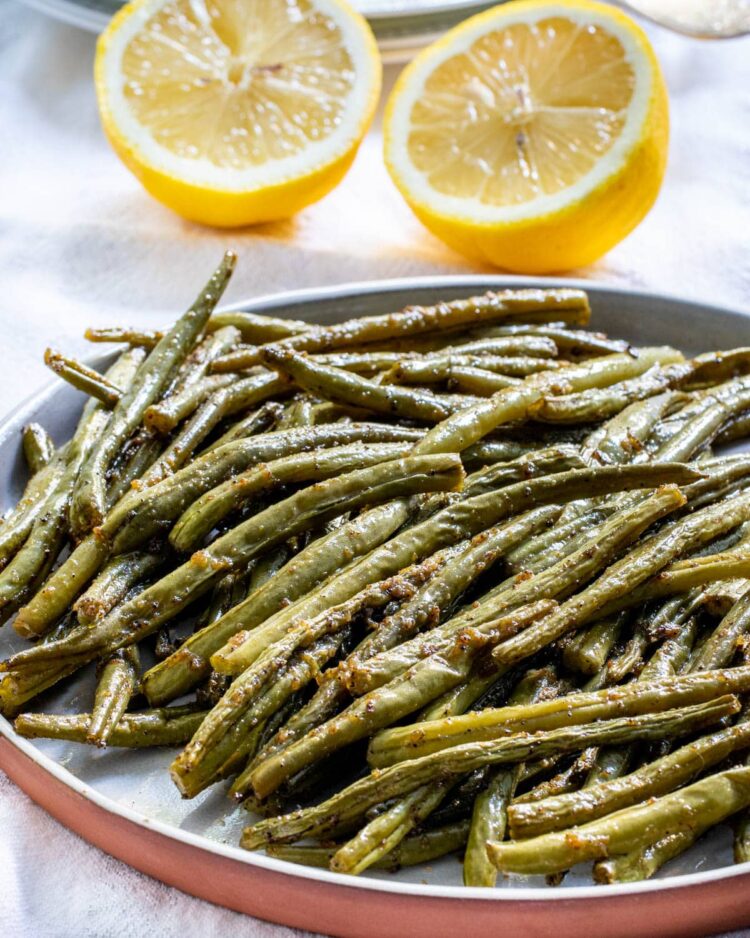 roasted green beans on a plate with 2 lemon halves in the background