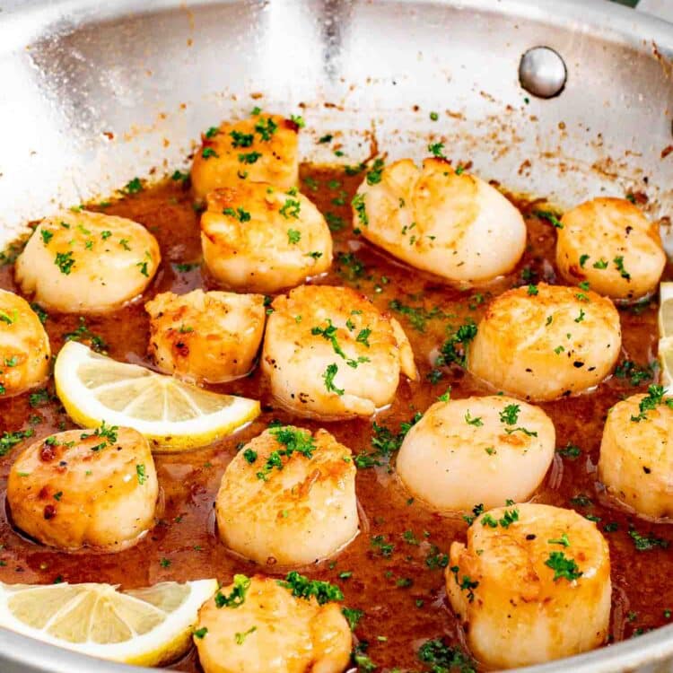 seared scallops in a skillet garnished with lemon wedges and parsley.