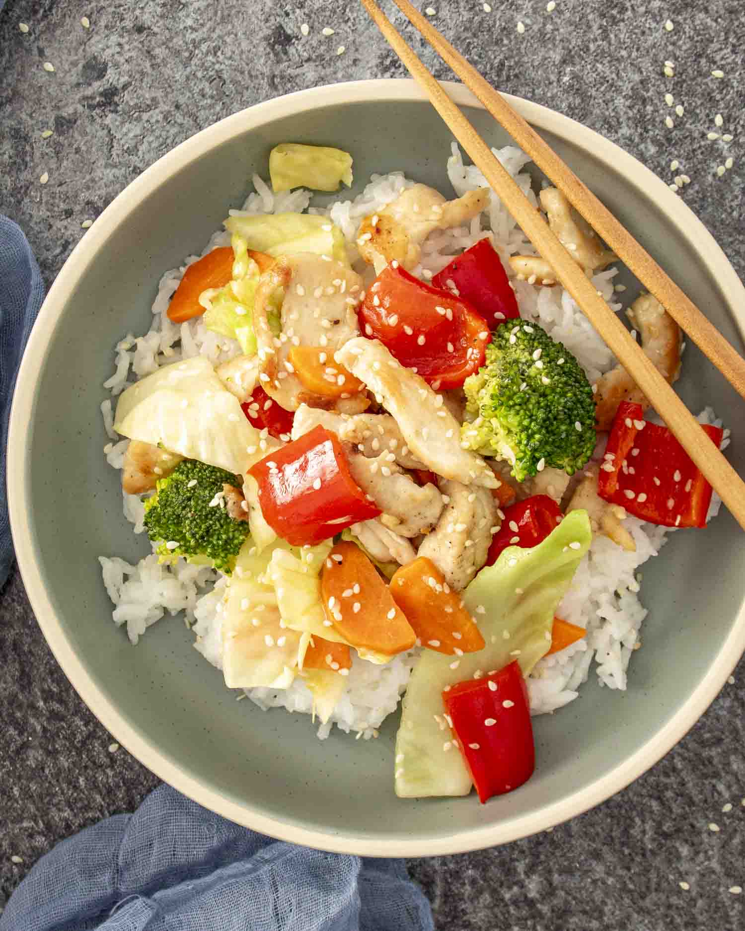 a serving of stir fried chicken and veggies in white sauce over a bed of rice in a bowl.