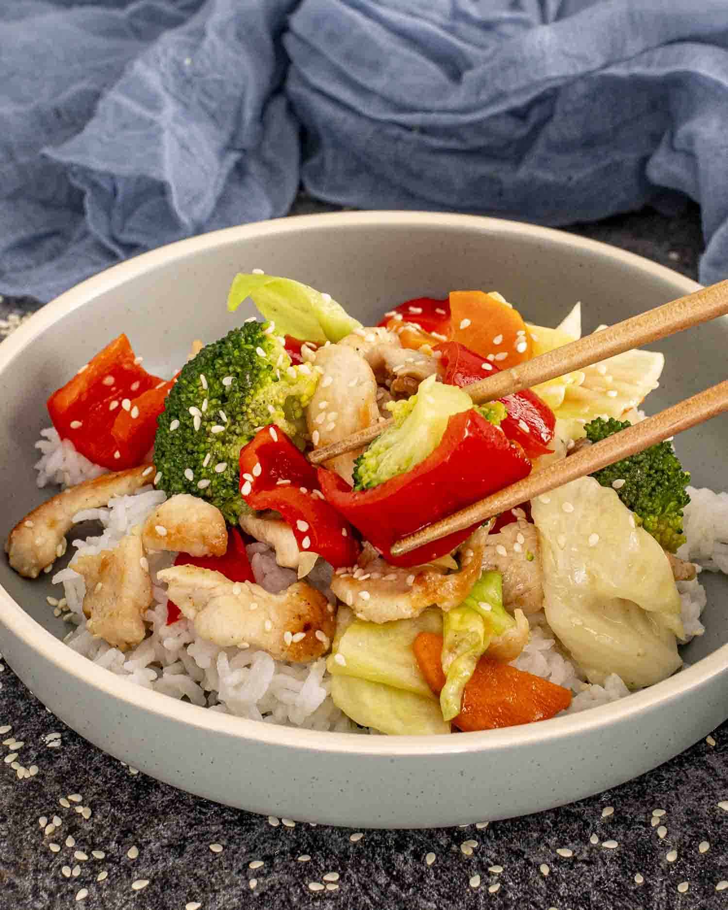 a serving of stir fried chicken and veggies in white sauce over a bed of rice in a bowl.
