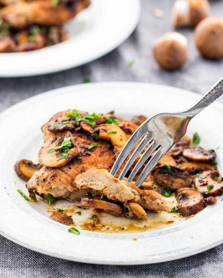 a fork holding a piece of chicken and mushrooms
