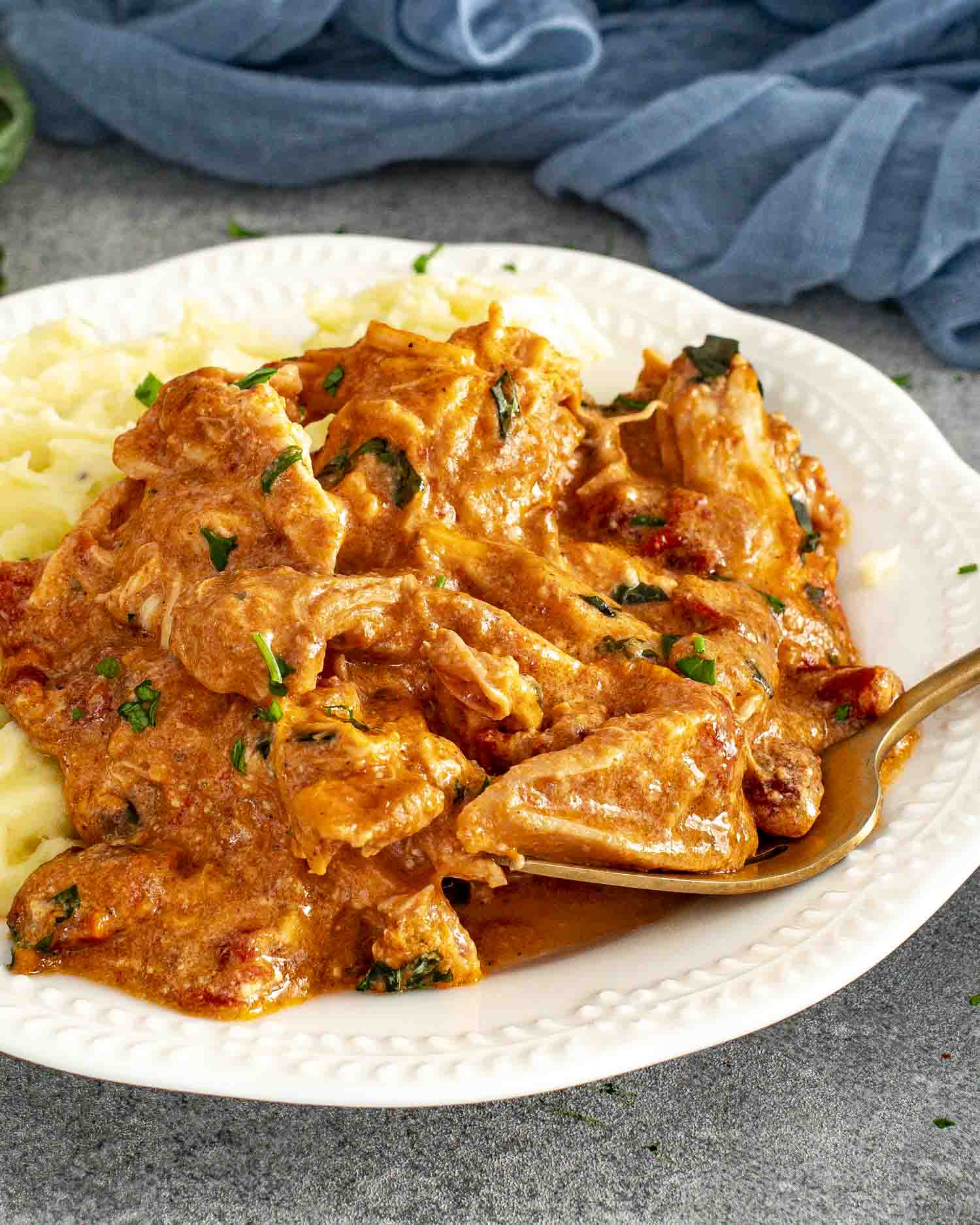 Shredded Marry Me Chicken served on a white plate with mashed potatoes and a fork, garnished with basil.