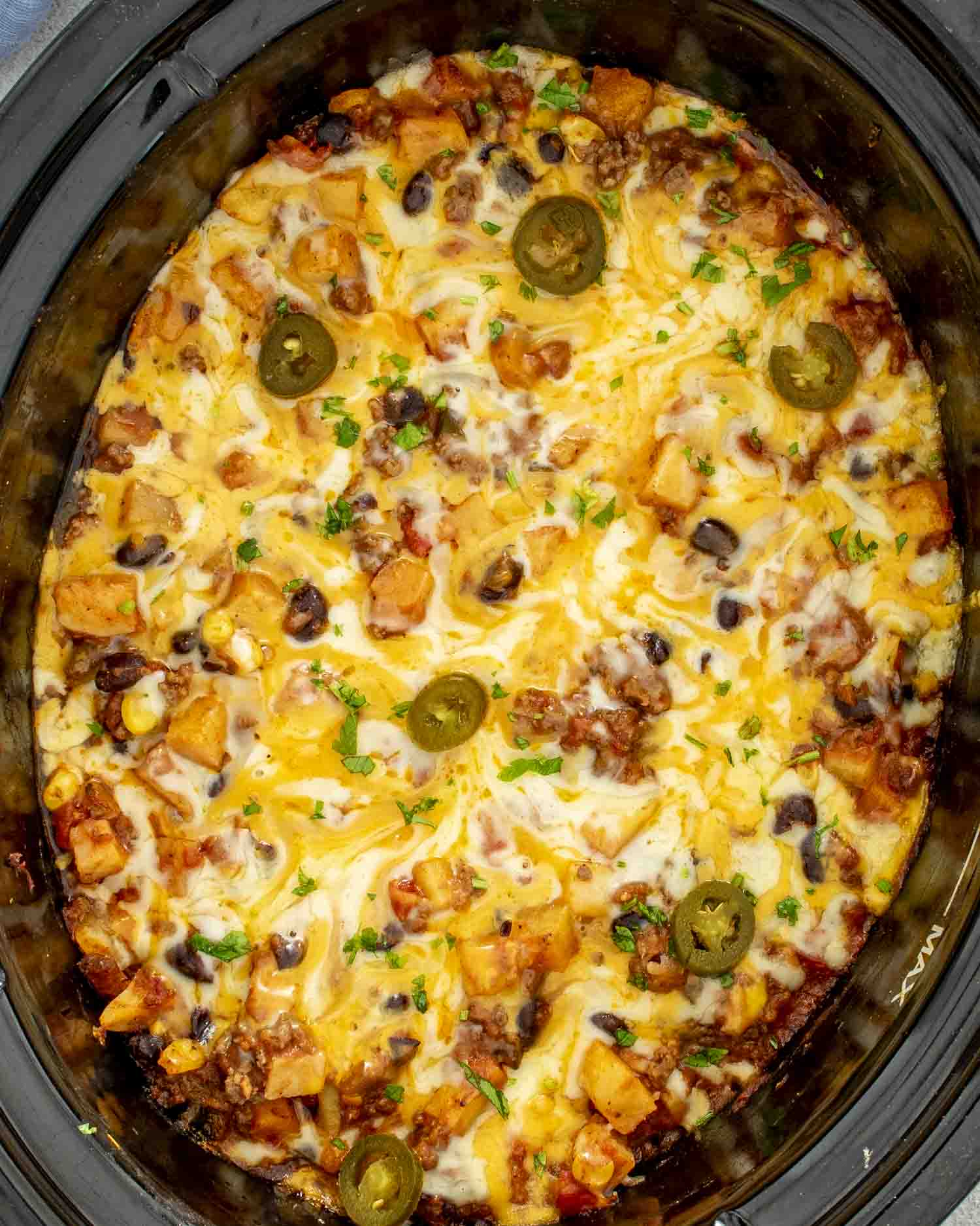 Overhead shot of cheesy taco casserole cooked in a slow cooker, topped with jalapeños and fresh parsley.