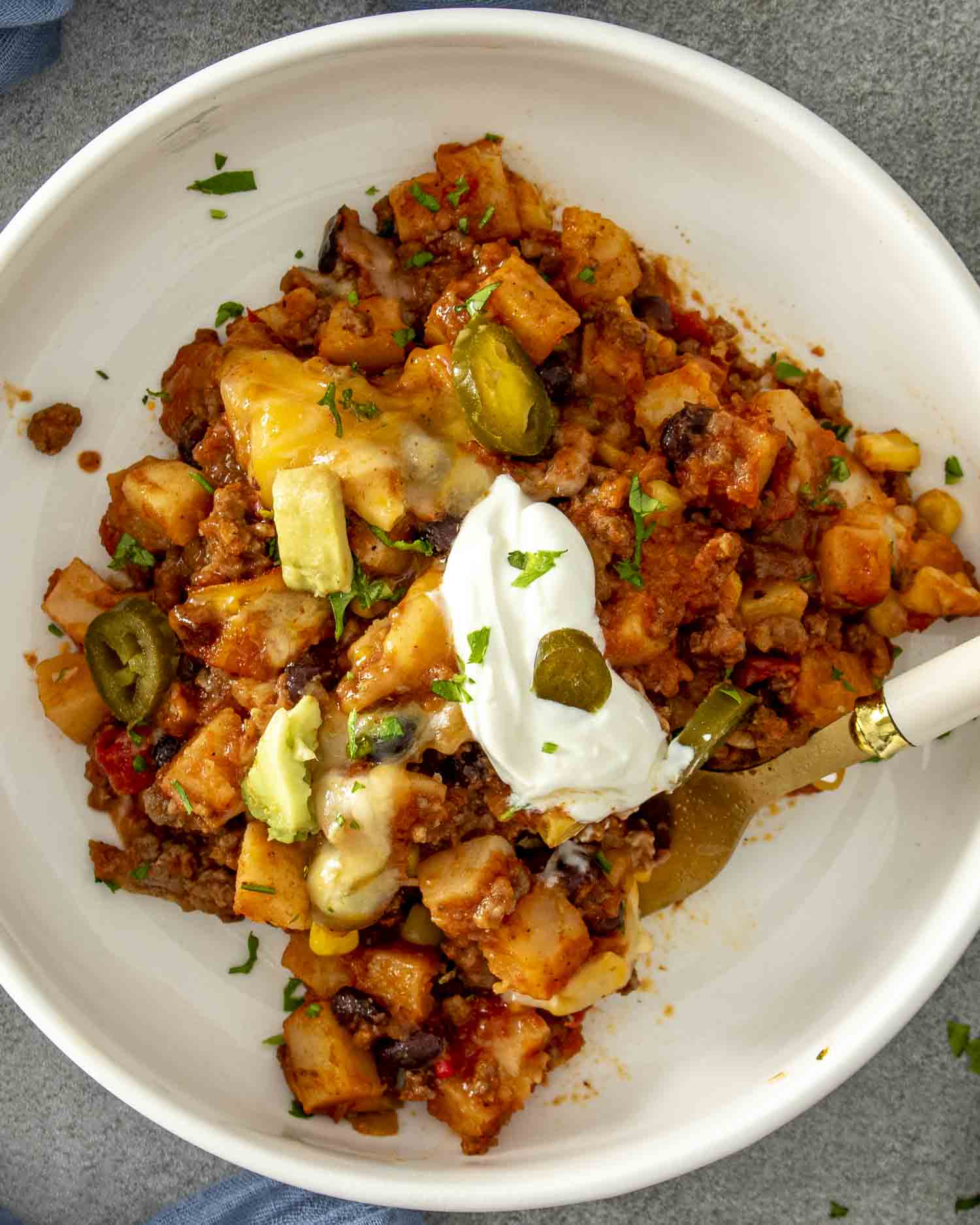 Top-down view of taco casserole in a white bowl, garnished with sour cream, jalapeños, and chopped cilantro.