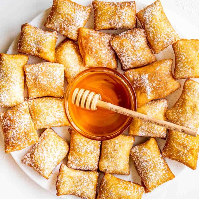 sopapillas on a big white plate with a bowl with honey in the middle.