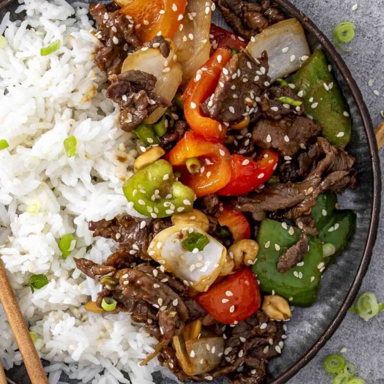 szechuan beef with rice on a plate garnished with sesame seeds.