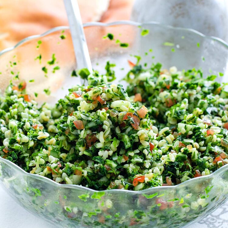 closeup of tabbouleh salad in a glass bowl with a spoon inside.