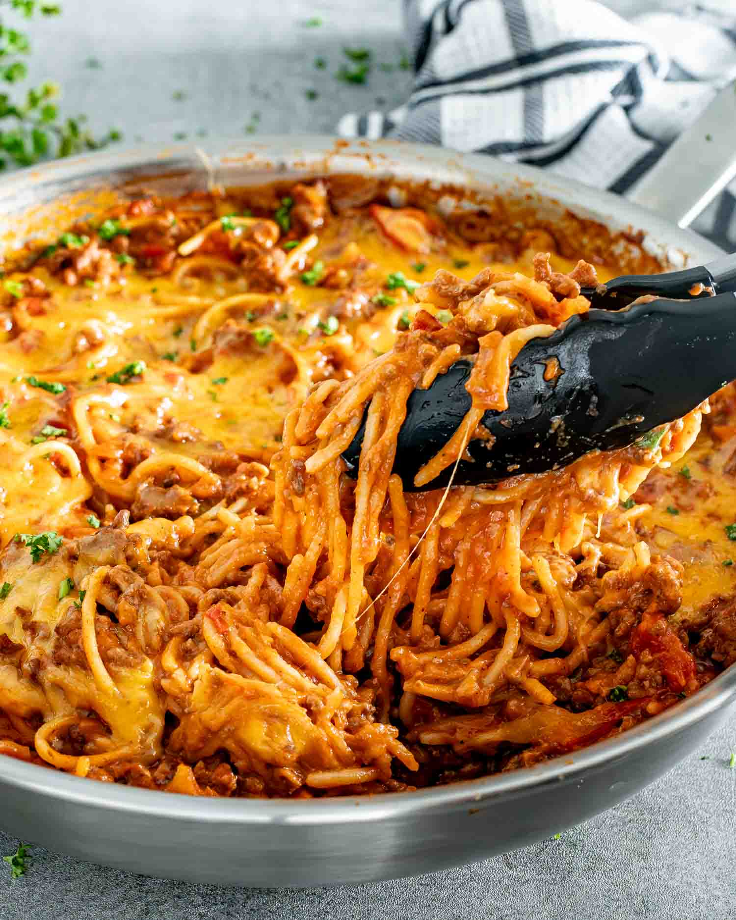 freshly made taco spaghetti in a stainless steel skillet topped with cheese and garnished with parsley.