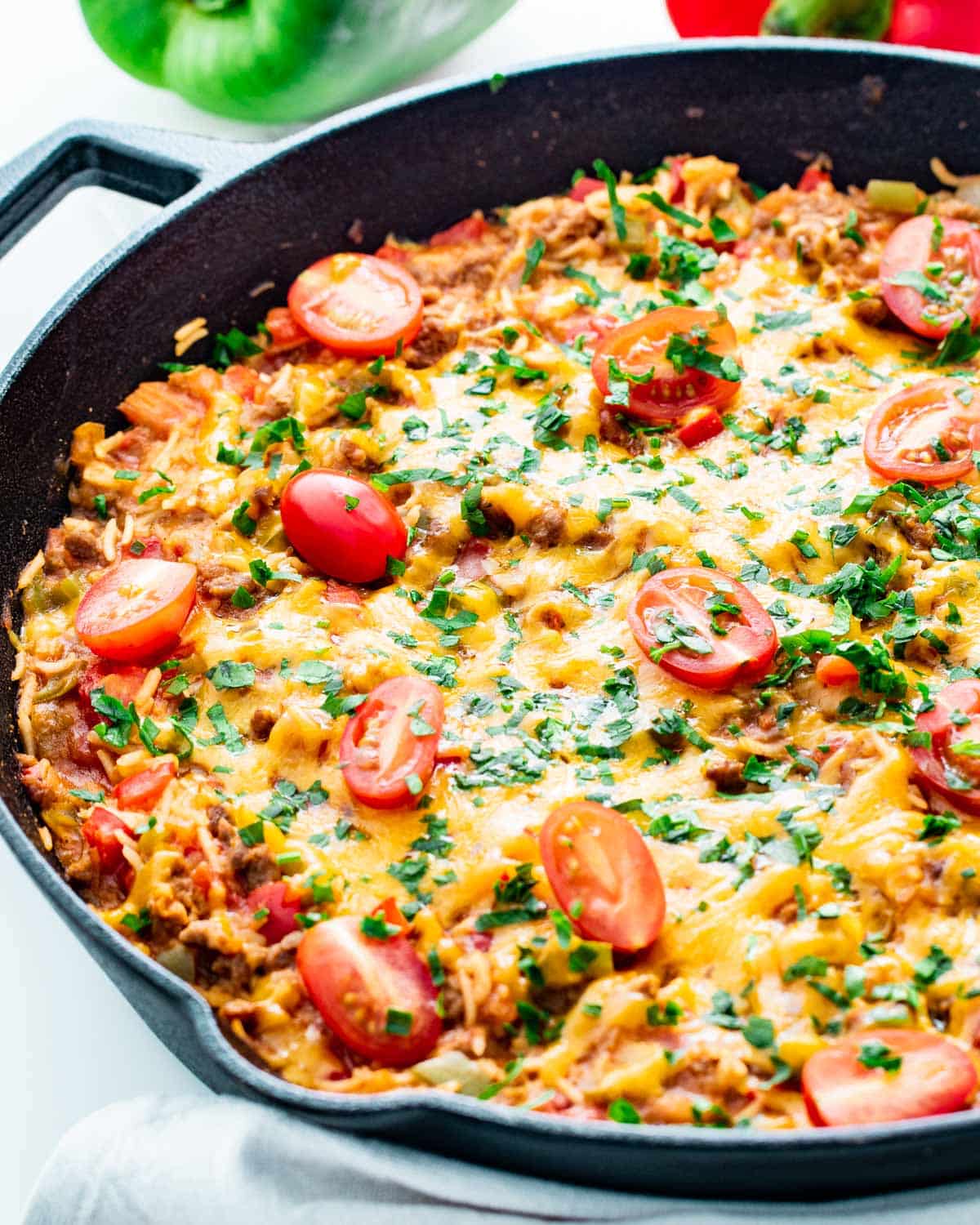 side view shot of taco stuffed pepper casserole in a black skillet garnished with tomatoes and cilantro
