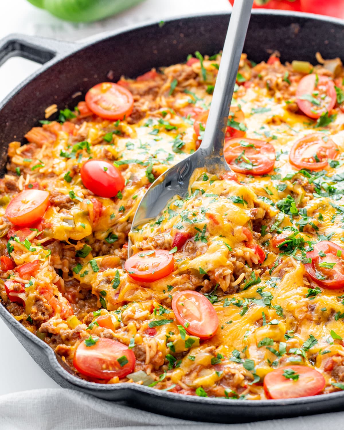 sideview shot of a serving spoon holding some stuffed pepper casserole in a black skillet