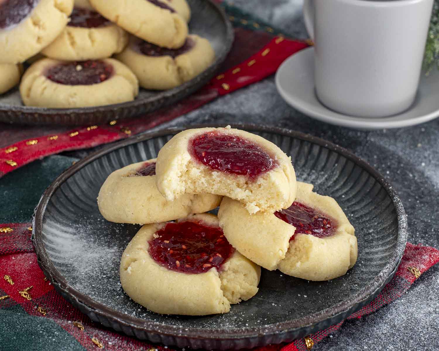 A bitten thumbprint cookie showing soft, tender texture and sweet jam center, stacked on a plate beside more cookies.