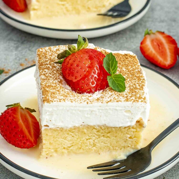 A close-up of a single slice of Tres Leches Cake, soaked perfectly, topped with cinnamon and a fresh strawberry.