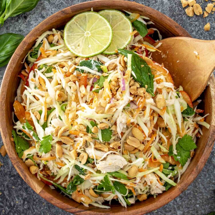 fresh vietnamese chicken salad in a wooden bowl garnished with 2 lime slices.