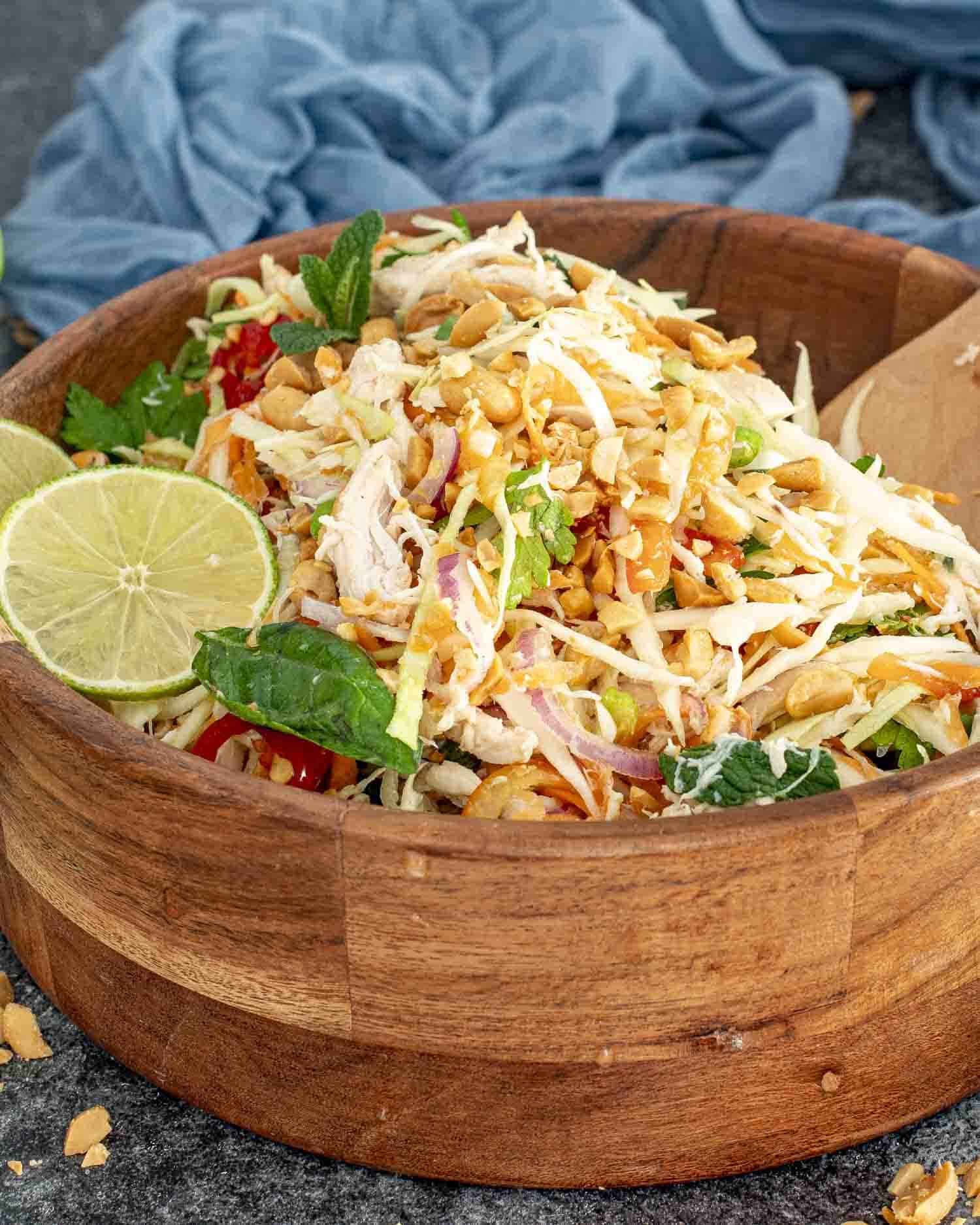 fresh vietnamese chicken salad in a wooden bowl garnished with 2 lime slices.