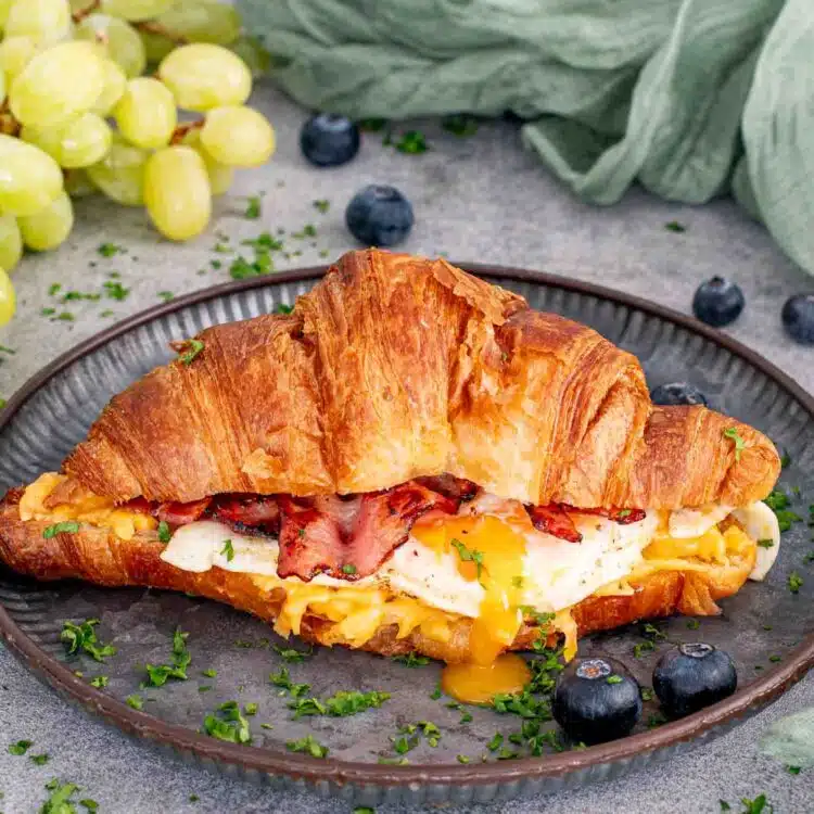 a bacon egg and cheese croissant on a plate.