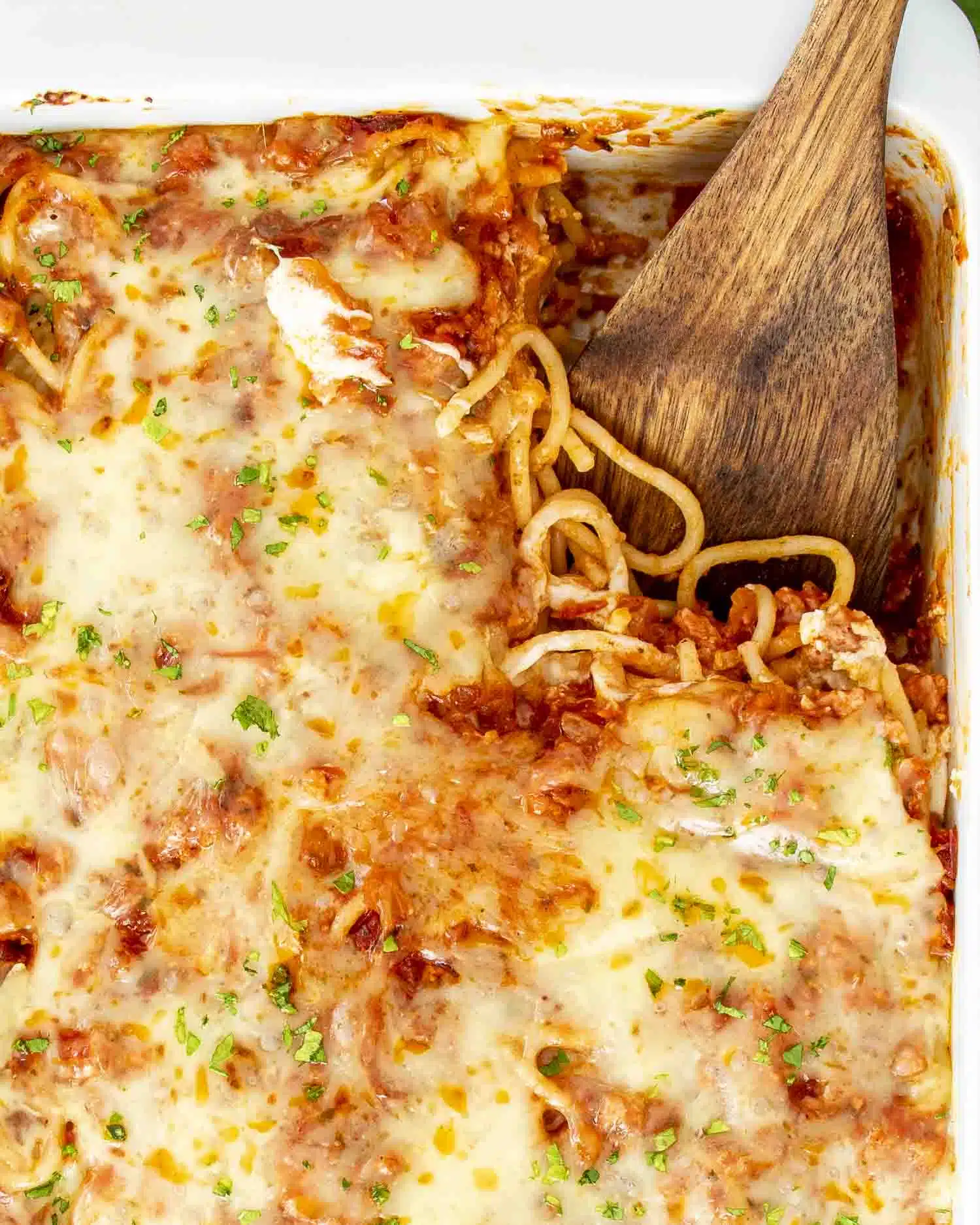 baked spaghetti garnished with parsley in a white casserole dish.