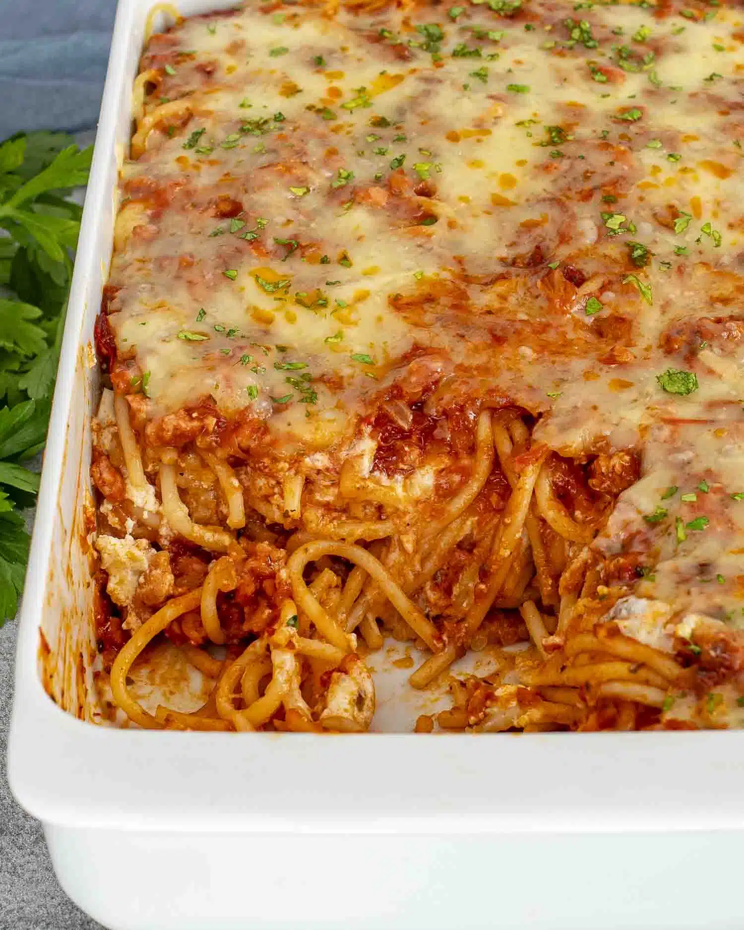 baked spaghetti garnished with parsley in a white casserole dish.