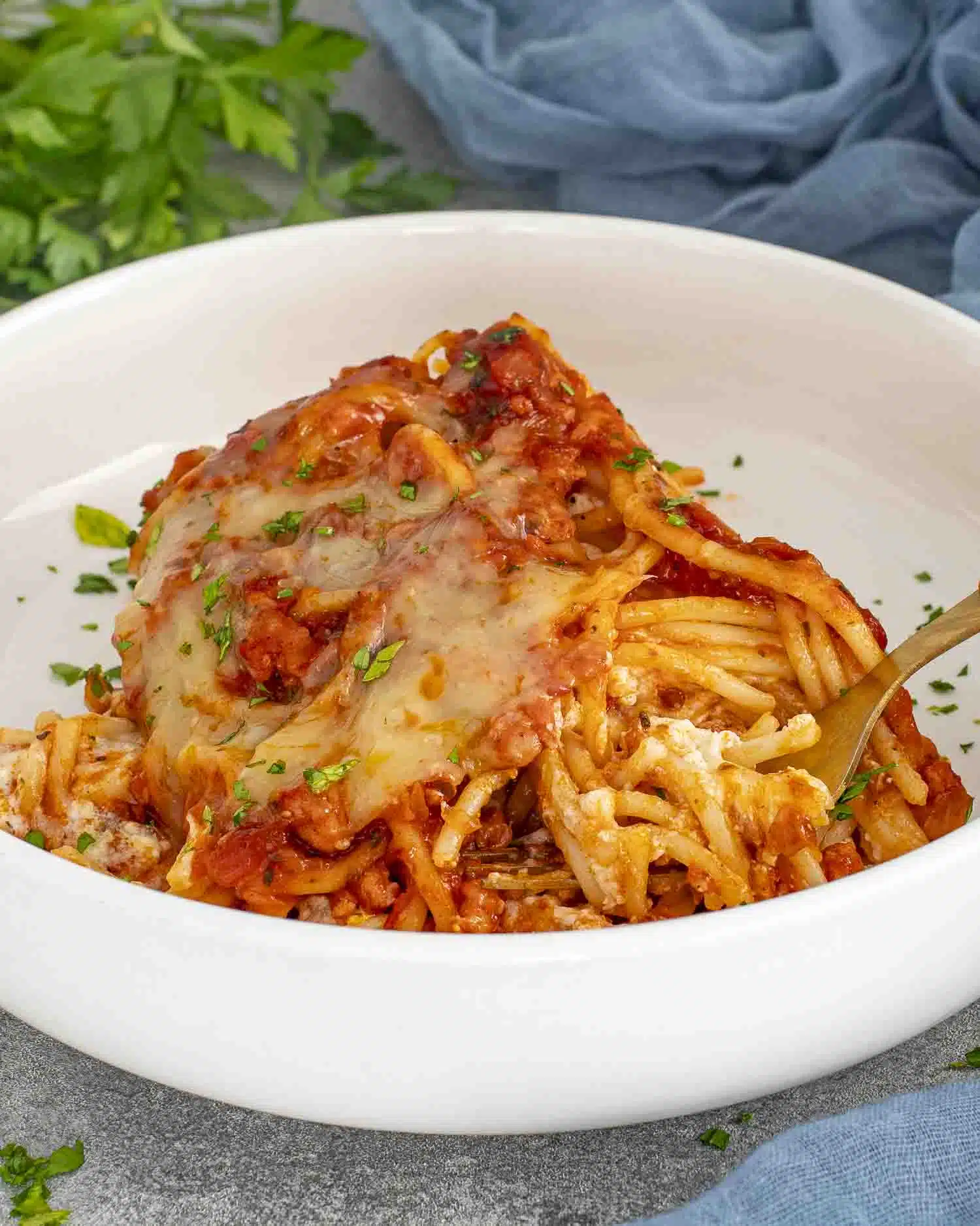 a white bowl with a serving of baked spaghetti garnished with parsley.